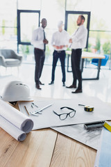 various architecture supplies on workplace with architects behind, focus on foreground