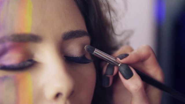 Closeup view of makeup artist makes models eye makeup with false eyelashes. Model with false lashes and face art painting preparing to the fashion show. Slowmotion shot.