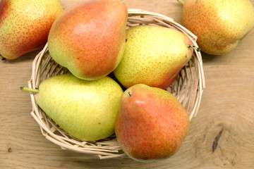 Red and yellow pears lays in small wicker straw basket on brown wooden table top view closeup
