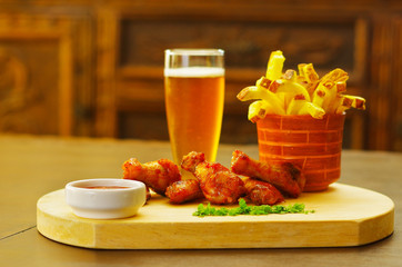 Delicious grilled chicken wings with ketchup and french fries and a glass of beer on wooden board