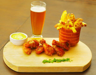 Delicious grilled chicken wings with french fries, ketchup, mustard and a glass of beer on wooden board