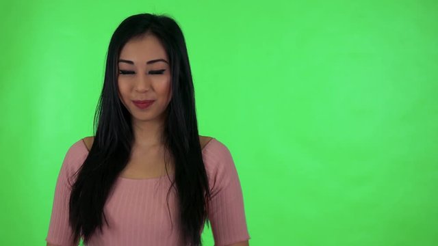 young attractive asian woman applauds and smiles to camera - green screen studio