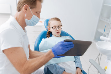 Fototapeta premium Bright attentive dentist showing updates on patients progress