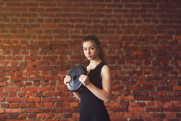 Young athlete exercising crossfit. Woman in sportswear doing crossfit workout on brick background.