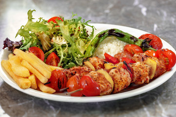 Chicken skewers, french fries and rice with leaf vegetable.