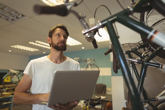 Thoughtful employee holding laptop at bicycle workshop
