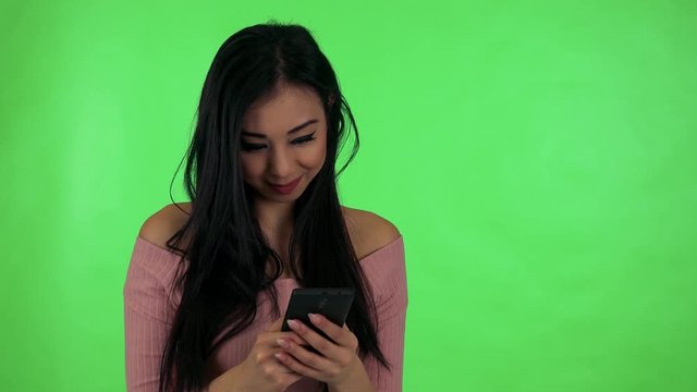 young attractive asian woman works on smartphone and smiles - green screen