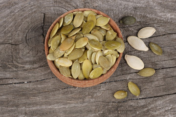 Pumpkin seeds in wooden bowl on wooden background top view with copy space