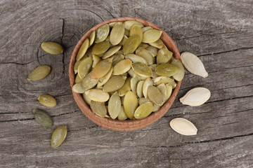 Pumpkin seeds in wooden bowl on wooden background top view with copy space