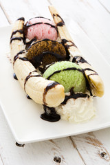 Banana split ice cream dessert with chocolate syrup on white wooden table
