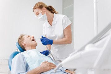 Pleasant mature gentleman having his teeth treated by professional