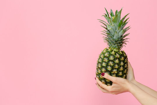 female hands holding pineapple on pink background