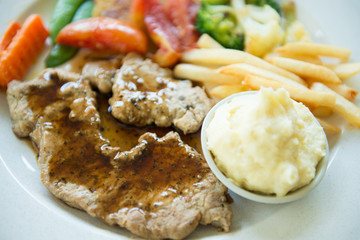 Black pepper pork steak served with mashed potatoes and vegetable on white plate