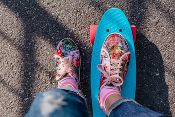 Close up of feet on blue penny skate board with pinl wheels.