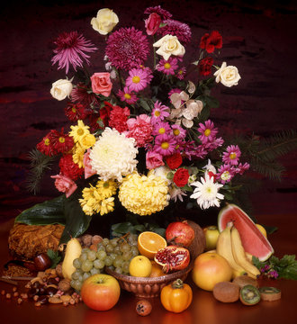 Assortment of citrus fruit, bananas, pomegranate, watermelon, grapes, coconut, nuts, autumn flowers, roses and geranium on a dark golden background