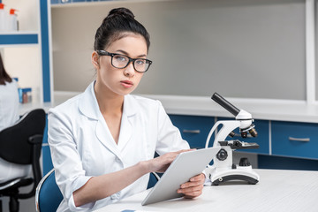 asian scientist in lab coat with microscope and digital tablet working in chemical lab