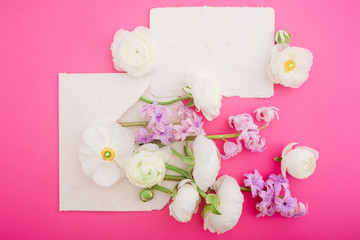 Beautiful flowers and paper cards on pink background. Flat lay, top view. Floral concept for wedding or beauty blog