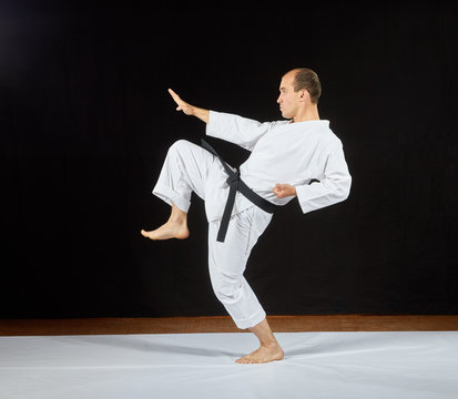 A man in karategi beats a kick leg on a black background