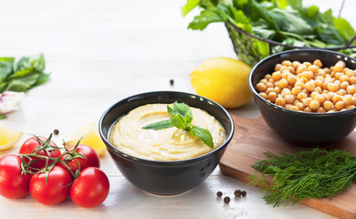 Bowl with hummus, chickpeas, lemon, cherry tomatoes and herbs on a white rustic wooden background. Middle Eastern cuisine. Background hummus with place for text.