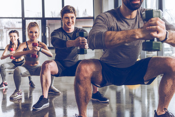 Group of athletic young people in sportswear with dumbbells exercising at the gym