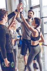 Happy young athletic people in sportswear giving high five in gym - obrazy, fototapety, plakaty