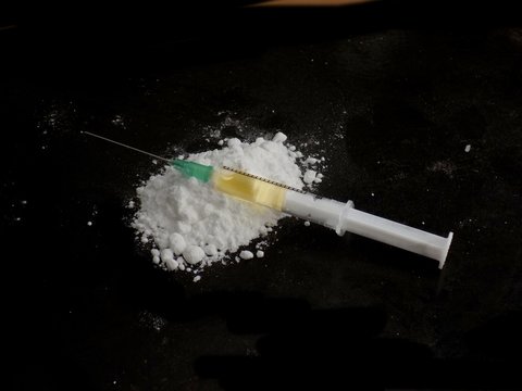 Injection syringe on cocaine drug powder on black background