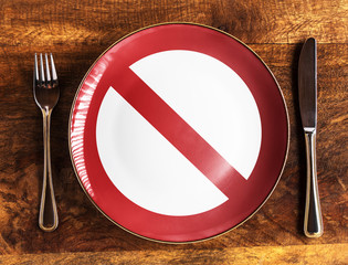 No food concept with forbidden symbol on plate with fork and knife on wooden table, overhead view