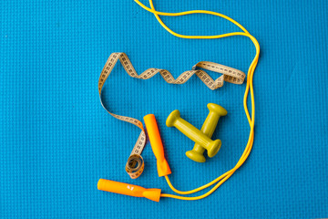 Fitness concept - yoga mat, dumbbells, skipping rope and tape measure