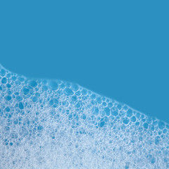 White soap bubbles foam isolated on blue background. Suds shower texture macro view photo