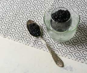 Fototapeta na wymiar Black caviar in a glass bowl with ice. Silver spoon and white background.
