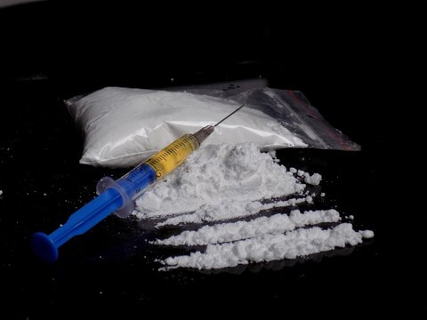 Injection syringe on cocaine drug powder lines and pile, cocaine bag on black background