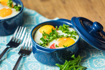 Baked eggs for breakfast in blue ceramic baking molds. Portioned casserole from vegetables and eggs in Italian style. Eggs Kokot
