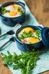Baked eggs for breakfast in blue ceramic baking molds. Portioned casserole from vegetables and eggs in Italian style. Eggs Kokot