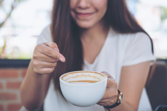 Closeup image of Asian woman holding and pointing at hot coffee with smiley face in coffee shop