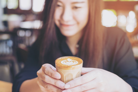 Closeup image of a beautiful Asian woman holding and showing hot coffee in vintage cafe