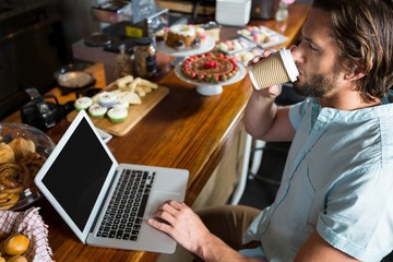 Man having coffee while using laptop at counter