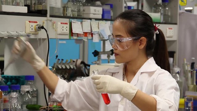 Female Scientist is Mixing red chemicals for research in laboratory.
