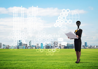 Camera headed woman standing on green grass against modern cityscape