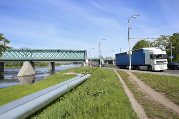 Fototapeta premium Transportation in city: railway bridge, industrial pipes and road transport. Kaunas, Lithuania – May 17, 2017: Industrial landscape with Green Railway Bridge.