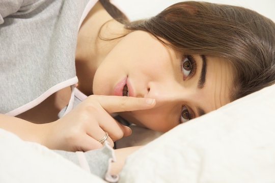 Young woman in bed making silence sign