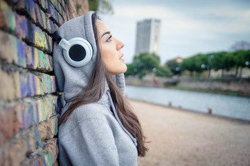 Young and sad woman listening music from her headphones outdoor - obrazy, fototapety, plakaty