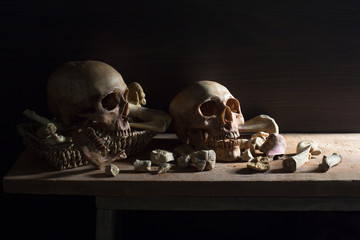 Two skulls and pile of bone on the plank with red candle light in dark night, Still life style and selective focus ..