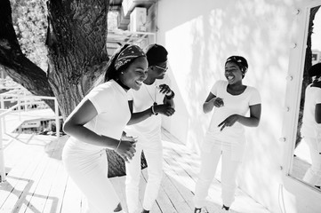 Fototapeta na wymiar Three stylish african american friends, wear on white clothes. Street fashion of young black people. Black man with two african girls dancing gangsta rap style.