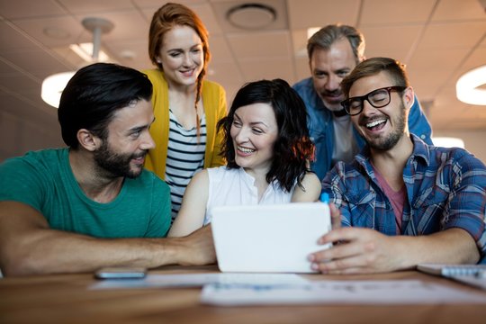 Happy creative business team discussing over digital tablet