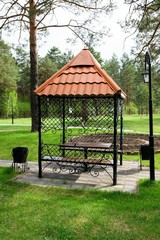 Black gazebo of wrought iron with a pattern and brown tiles in the park on the lawn.