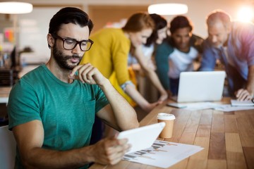 Man using digital tablet while team working in background
