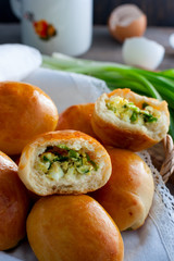 Oven fresh home made baked patties stuffed with eggs and green onion on rustic wooden background. Home cuisine. Close up delicious stuffed home cooking pastries on an orange plate and napkin.