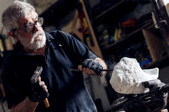 Senior Sculptor Working On His Marble Sculpture In His Workshop With Hammer And Chisel.