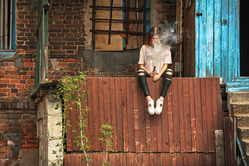 Beautiful vape teenager. Portrait of a pretty young white girl with red curly hair vaping an...