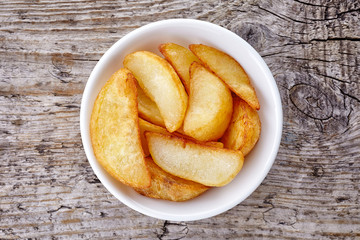 Bowl of potato wedges on wood, from above